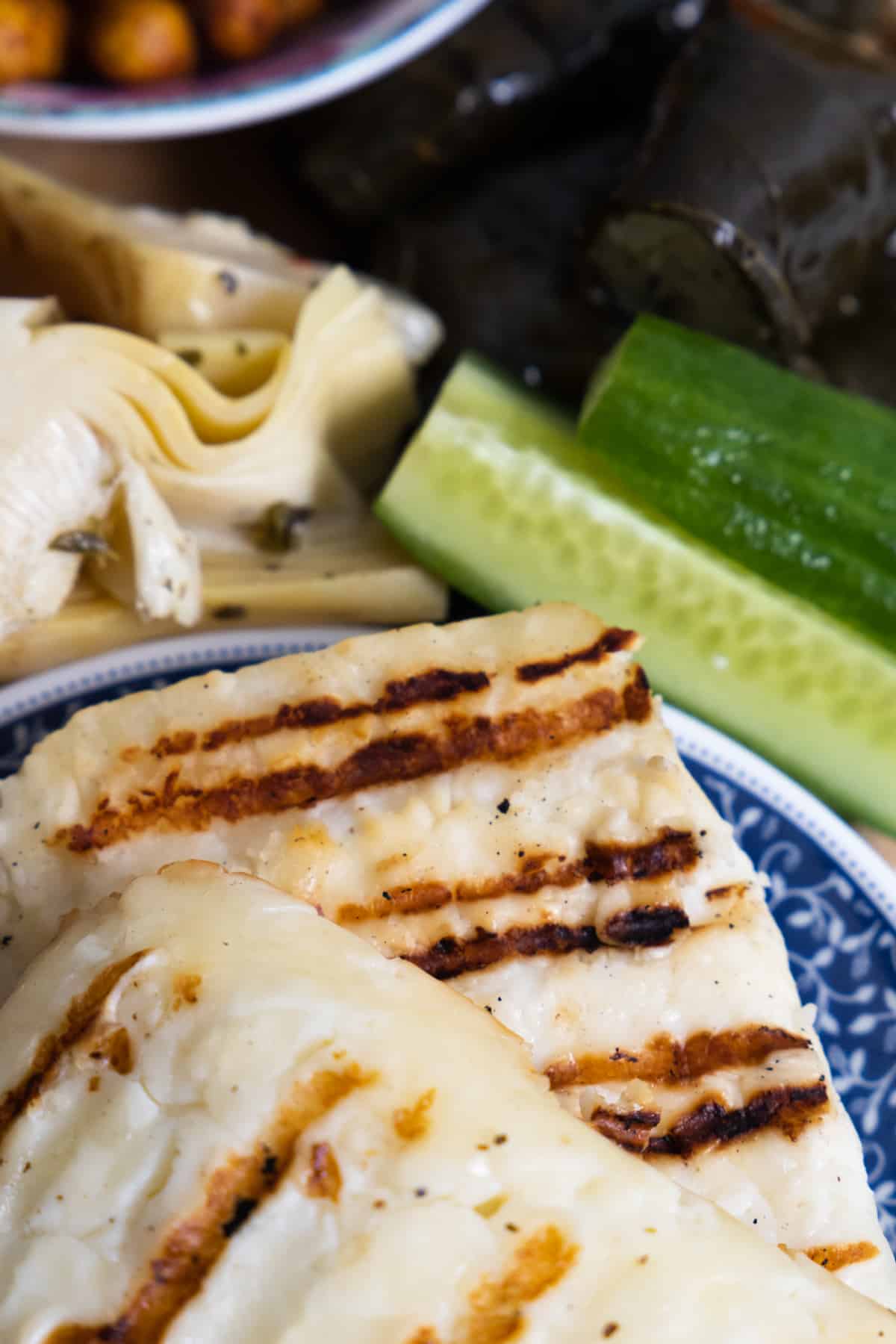 Close up of grilled halloumi with sliced cucumber in the back. 