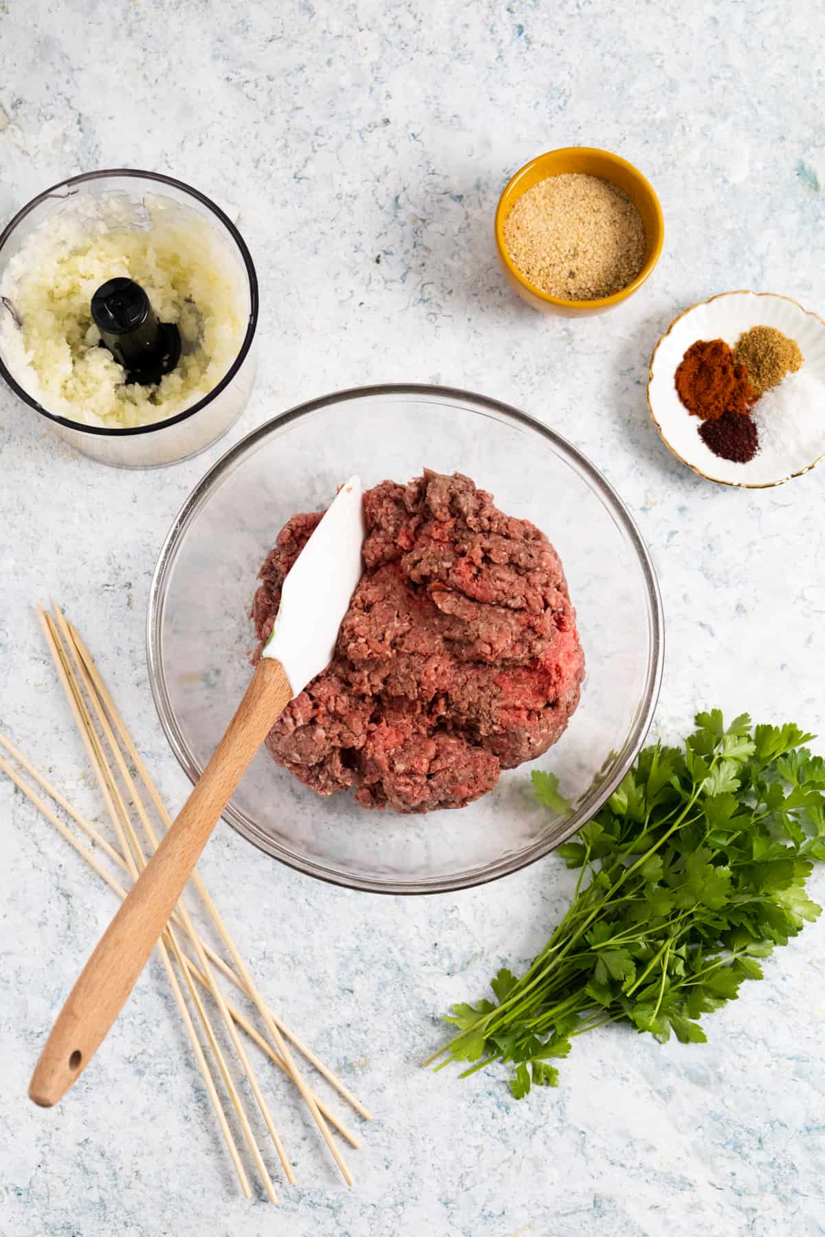 Ground lamp in a transparent mixing bowl, wood skewers on the side and spices in a small white plate.