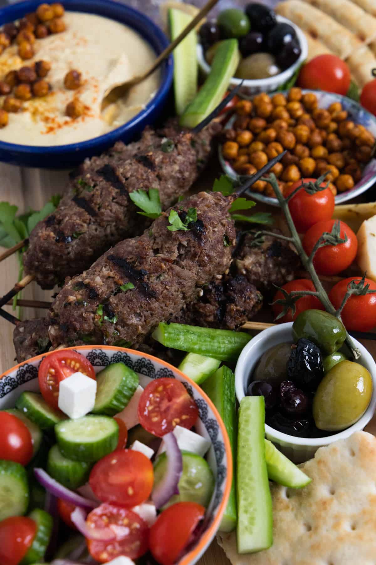 Koftas, cherry tomatoes on vine, hummus in the back and a tomato cucumber salad in a small at the bottom.