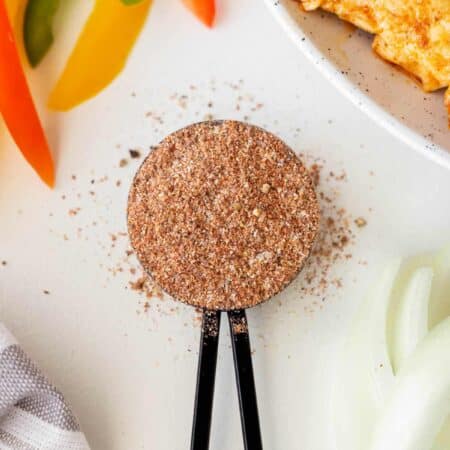 Overhead of a tablespoon of Fajita seasoning with sliced peppers and cooked seasoned chicken.