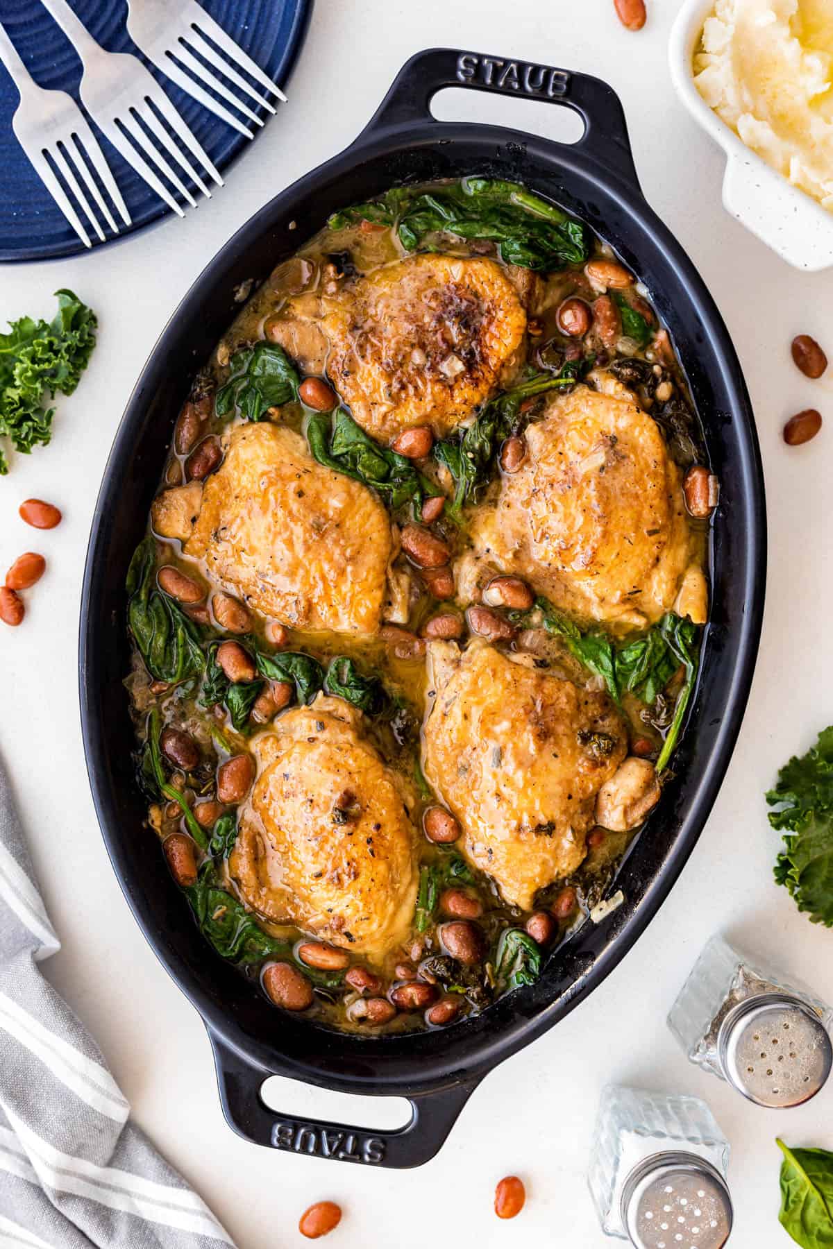 Overhead of chicken thighs in a casserole dish with beans and greens in a sauce. 