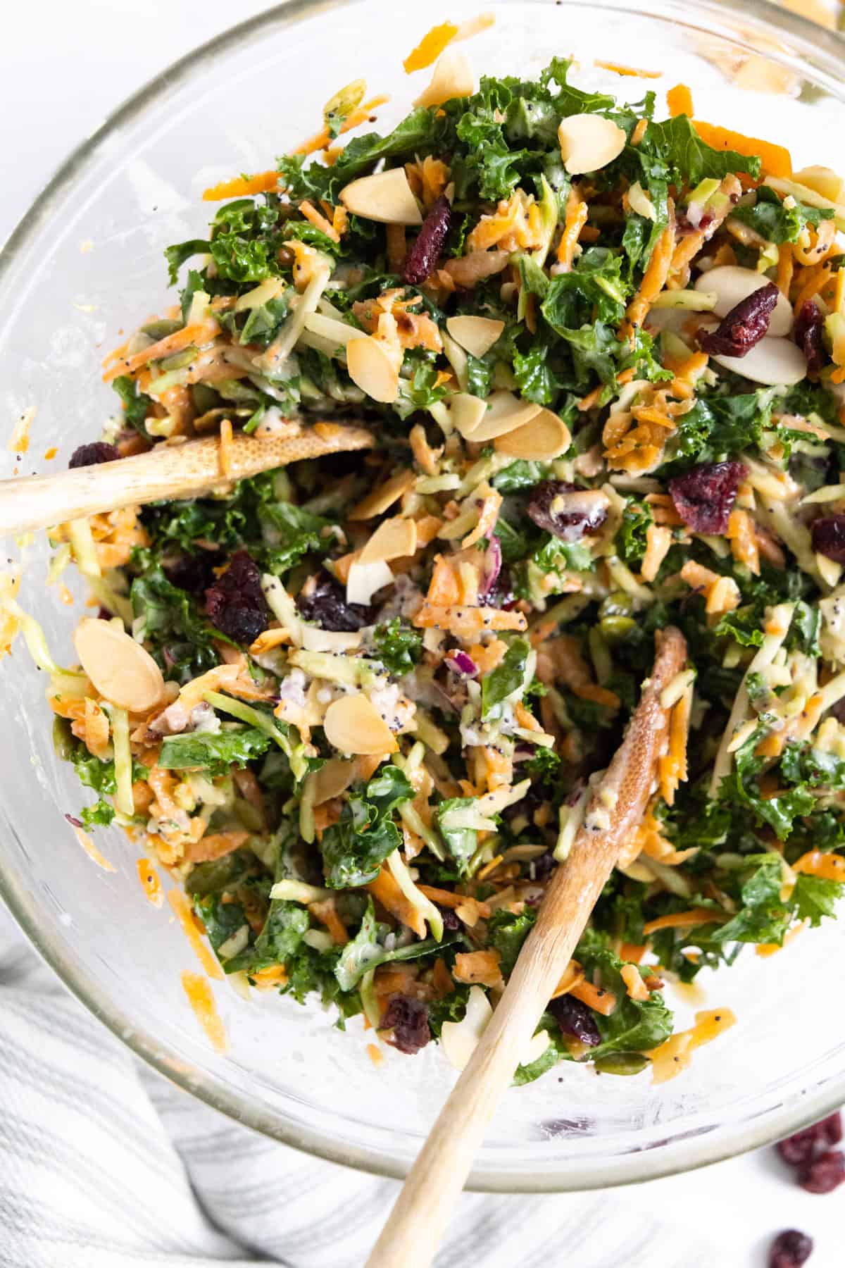 Kale salad in a transparent bowl with wooden spoon tucked in.