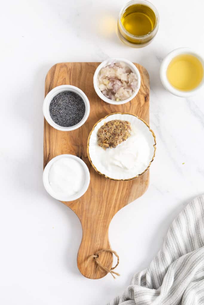 rectangular wood chopping board with small ramekins with poppyseeds, oil, vinegar. 