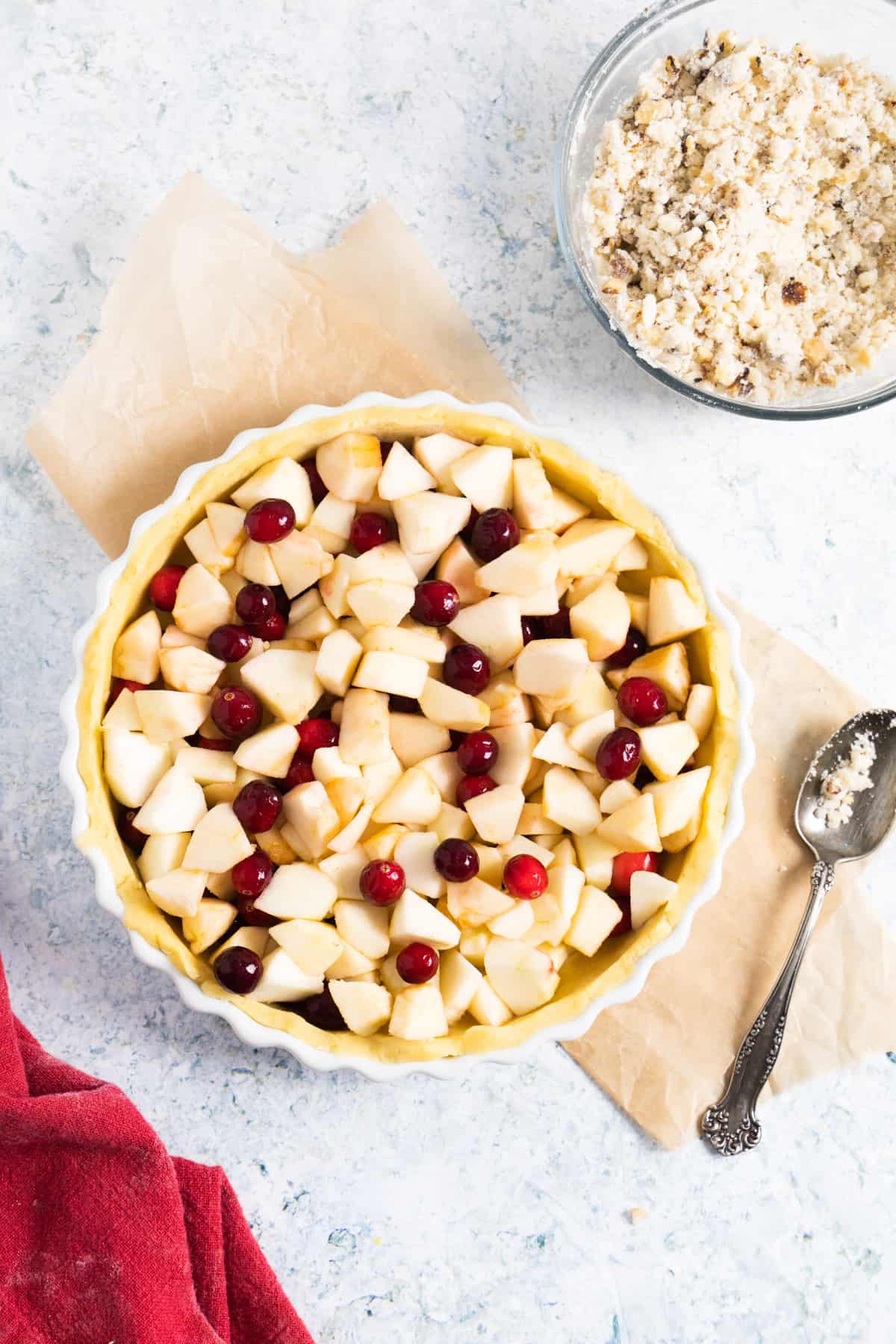 uncooked pie in a pie dish with cubed apples and cranberries as a filling a small bowl with crumbles on the side. 