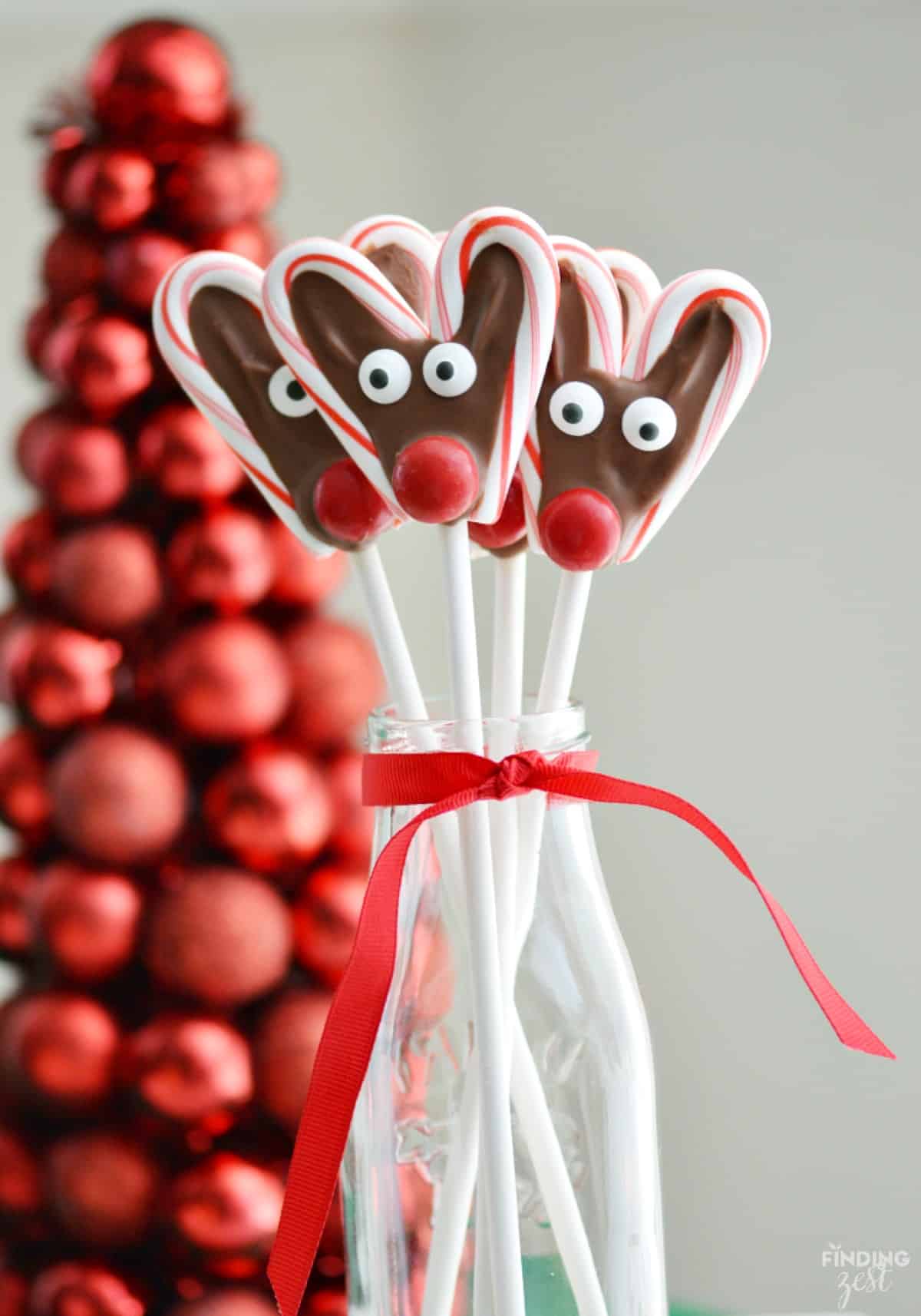 Candy Cane Reindeer Pops with the sticks in a clear glass jar with a red ribbon around the top of the jar.