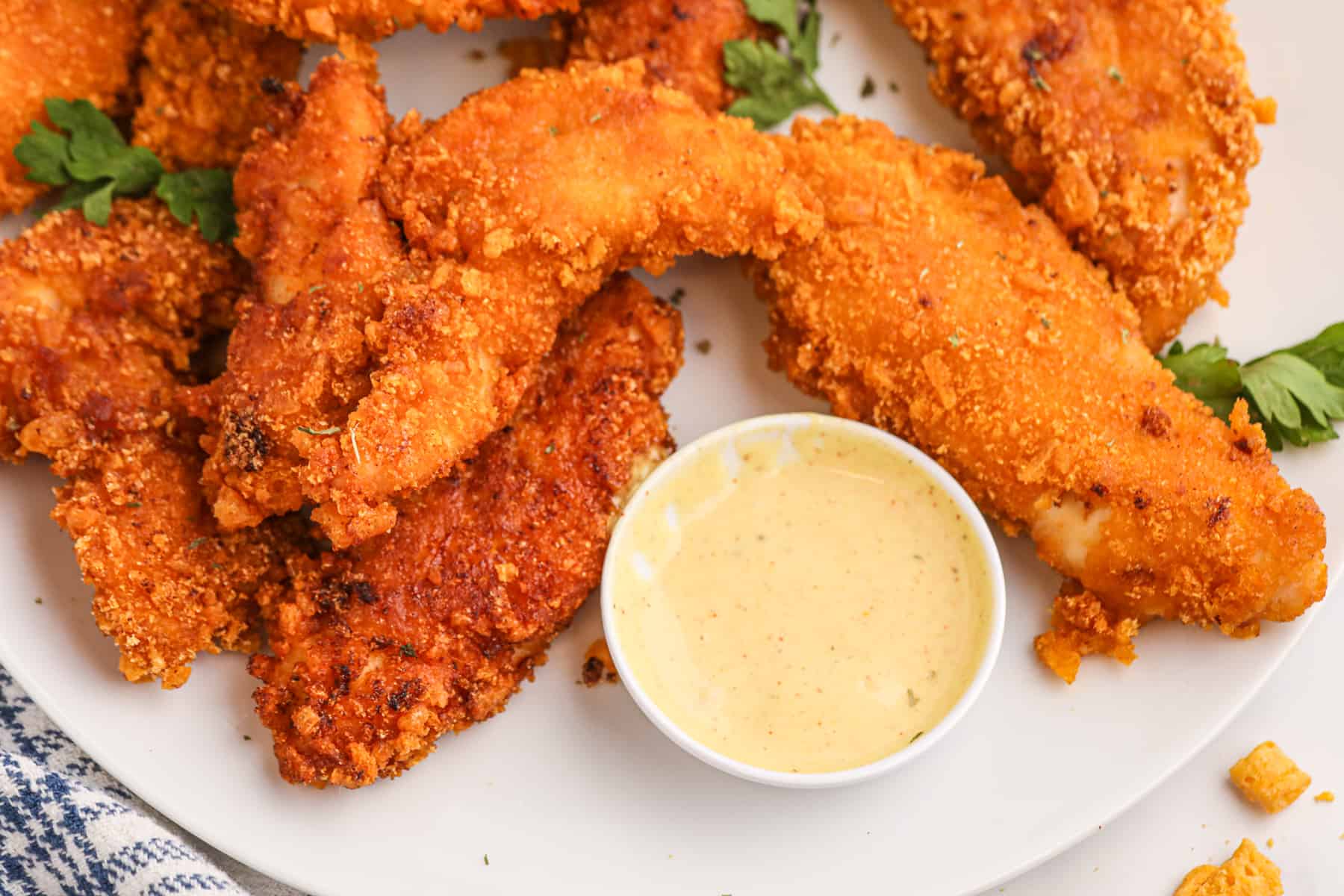 Overhead of chicken fingers on a plate with dipping sauce in a small bowl. 