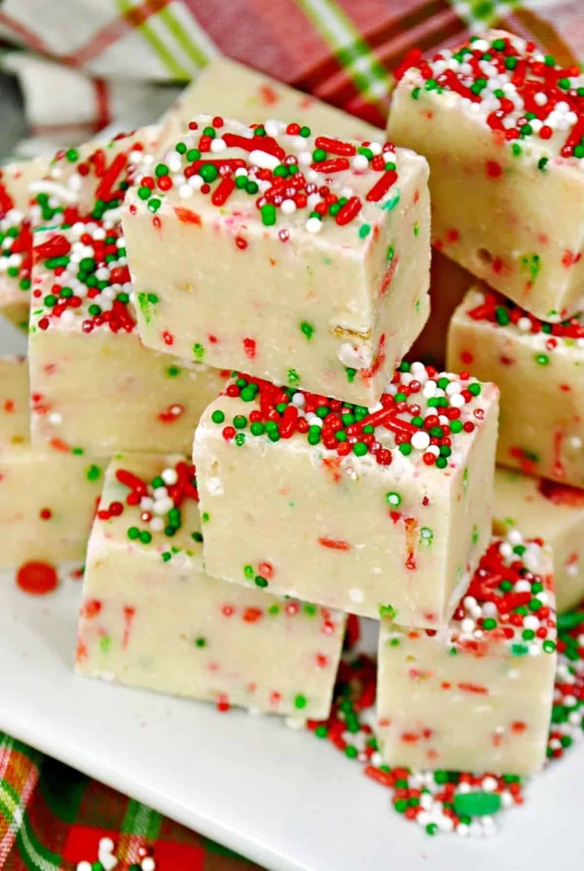 Squares of Sugar Cookie Christmas Fudge Stacked on top of a white platter.