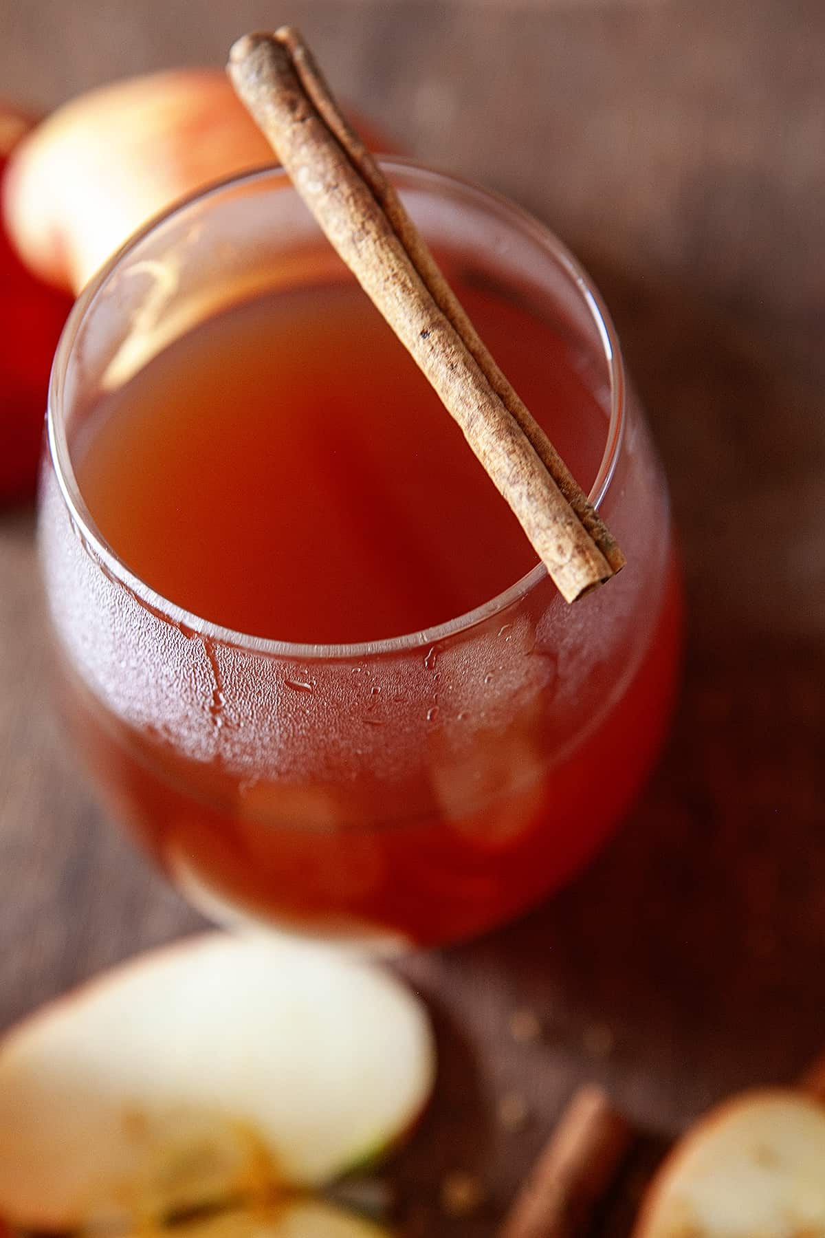 Slight overhead view and close-up of a glass of hot apple cider with a cinnamon stick on top of the glass.