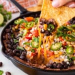 Taking a large dip of black bean dip on a tortilla chip.