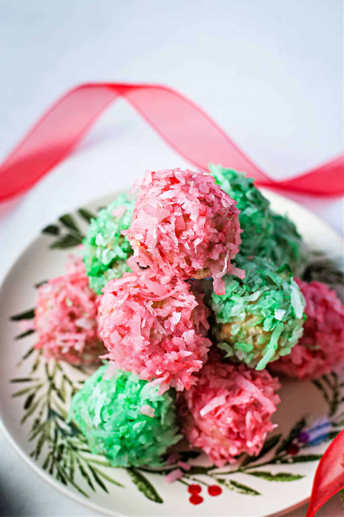 Homemade Coconut Balls in bright green and red colors on a plate with a Christmas design.
