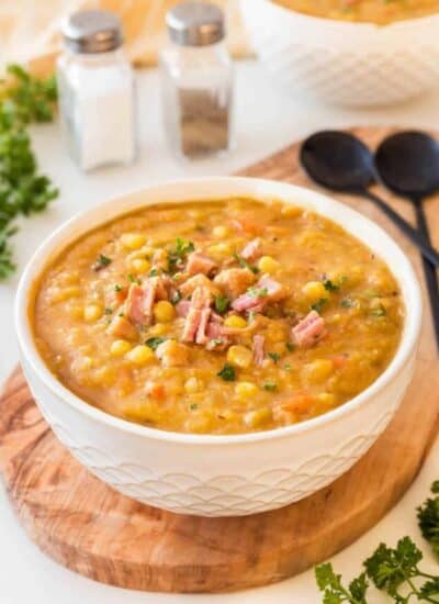 Split Pea Soup with Ham in a white bowl on a board with black spoon, salt and pepper in the background.