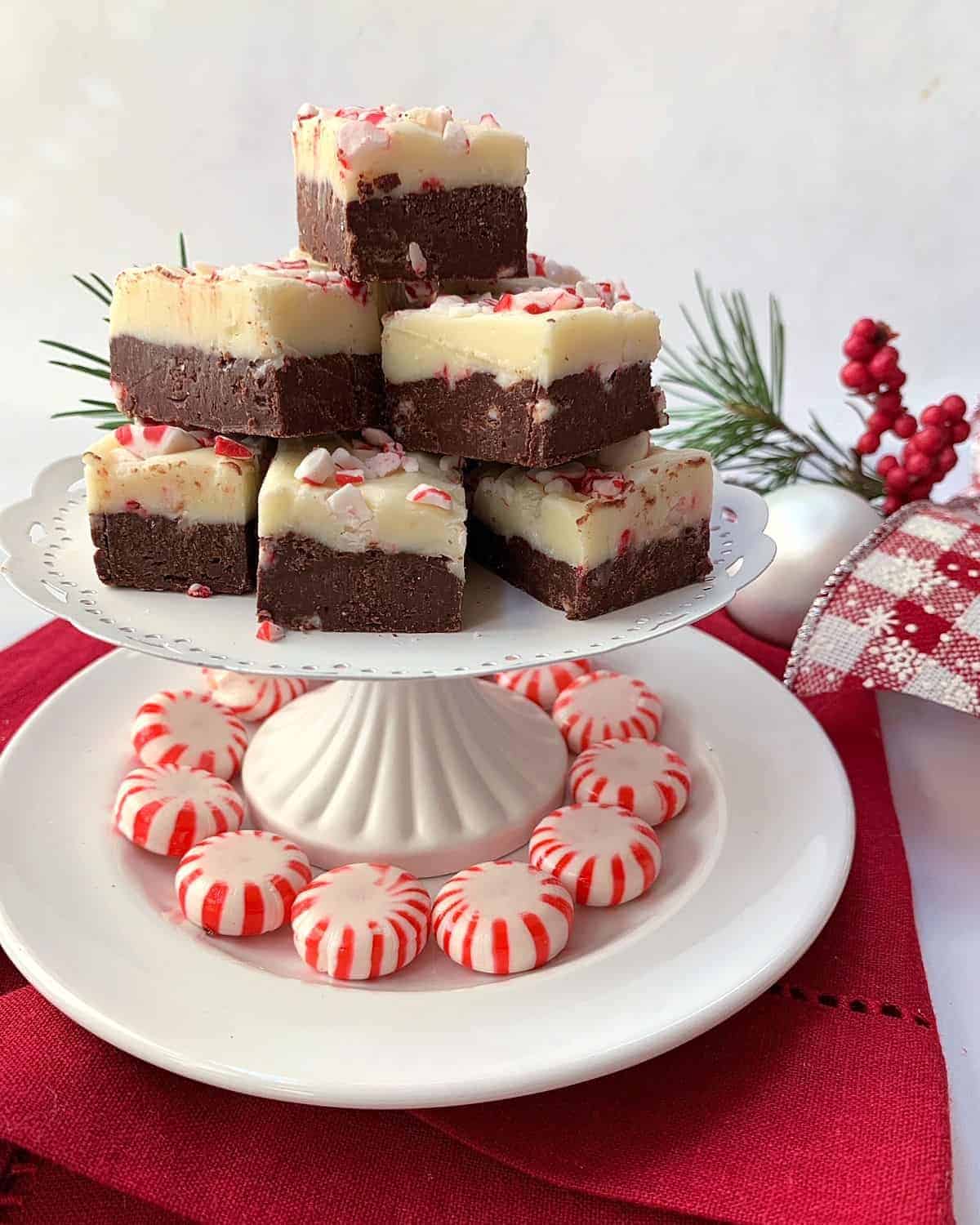 Layered Chocolate Peppermint Fudge stacked on a pedestal serving dish with peppermints around the bottom.