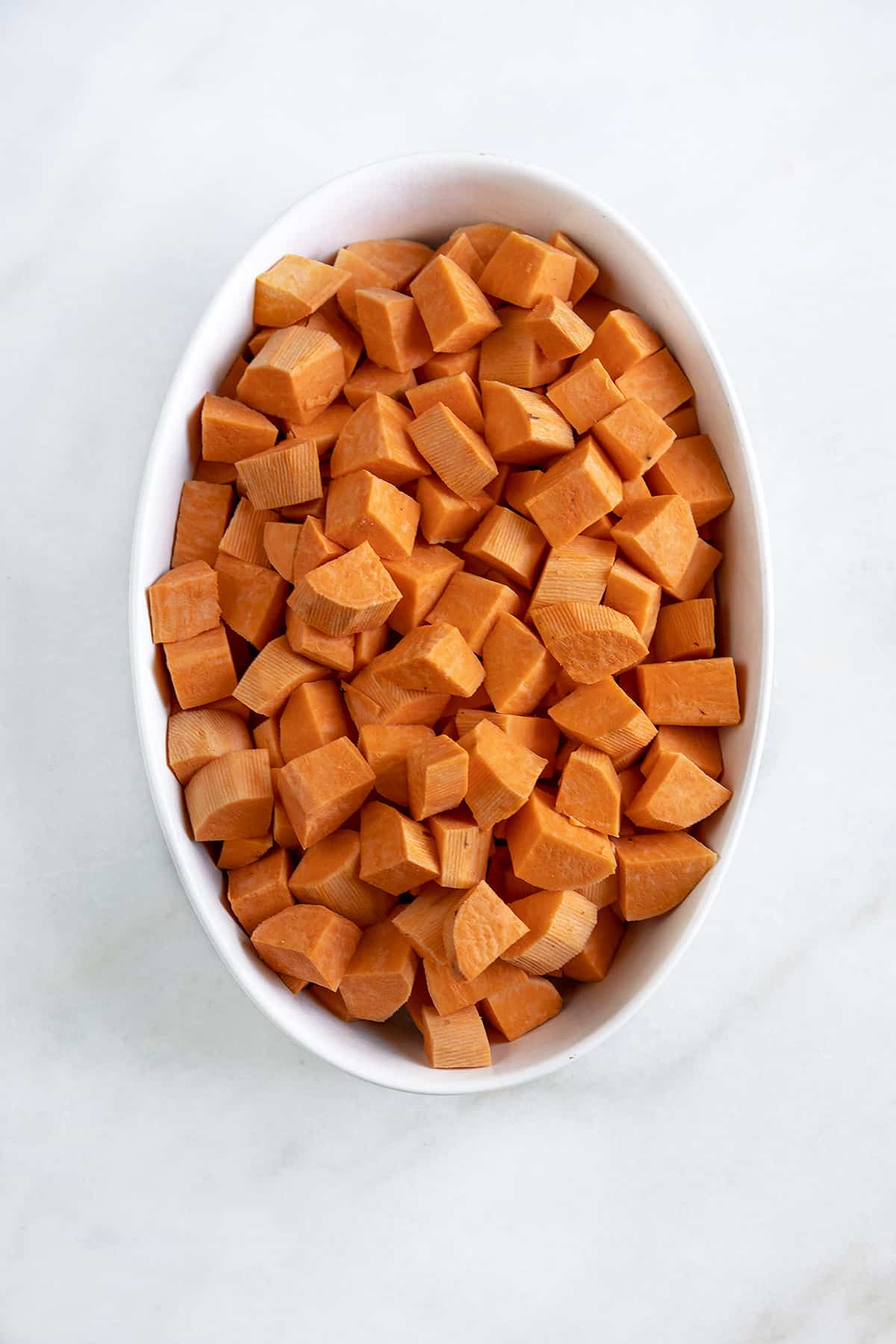 Cubed uncooked yam in a white oval casserole, overhead shot. 