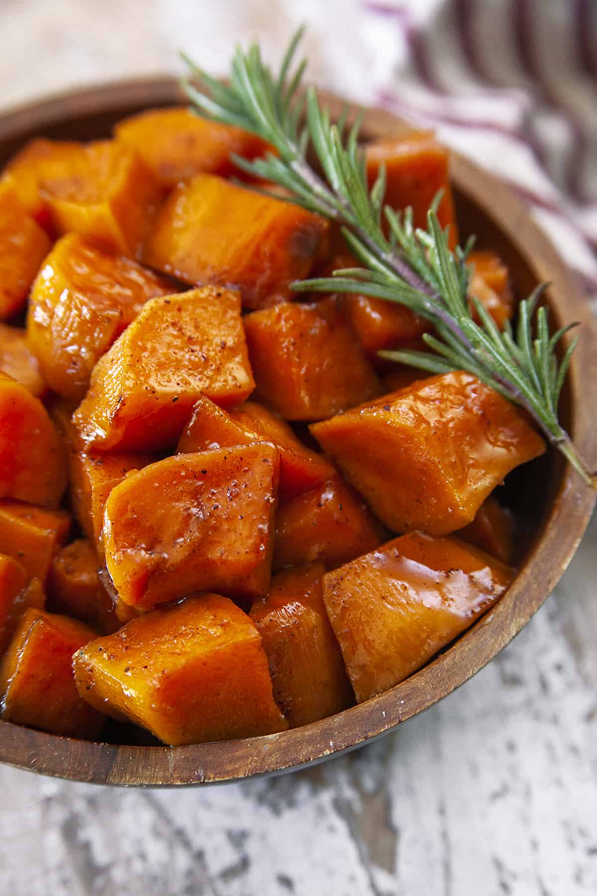 Candied yams with a sprig of rosemary in a wooden bowl. 
