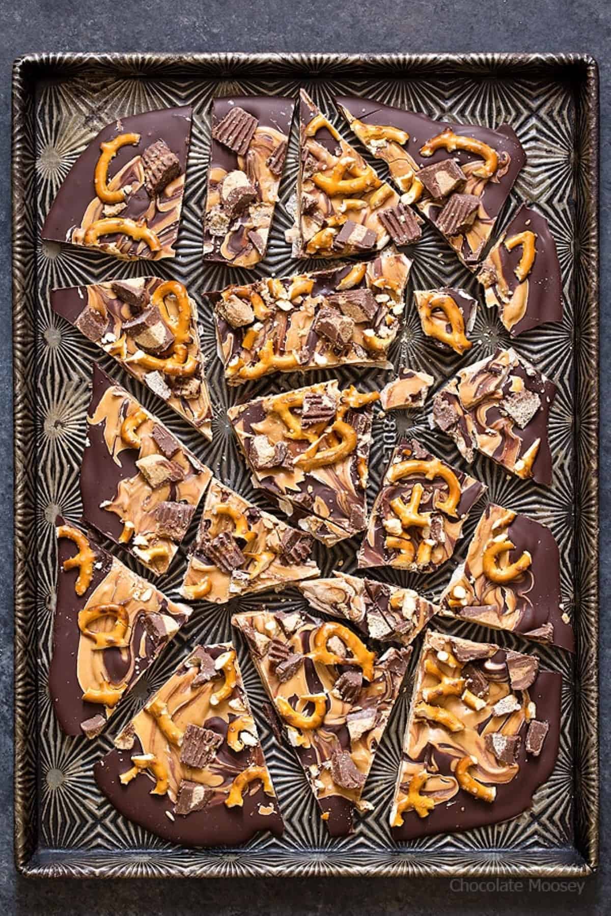 Chocolate Peanut Butter Pretzel Bark broken into pieces on a large metal tray with a black and silver design.