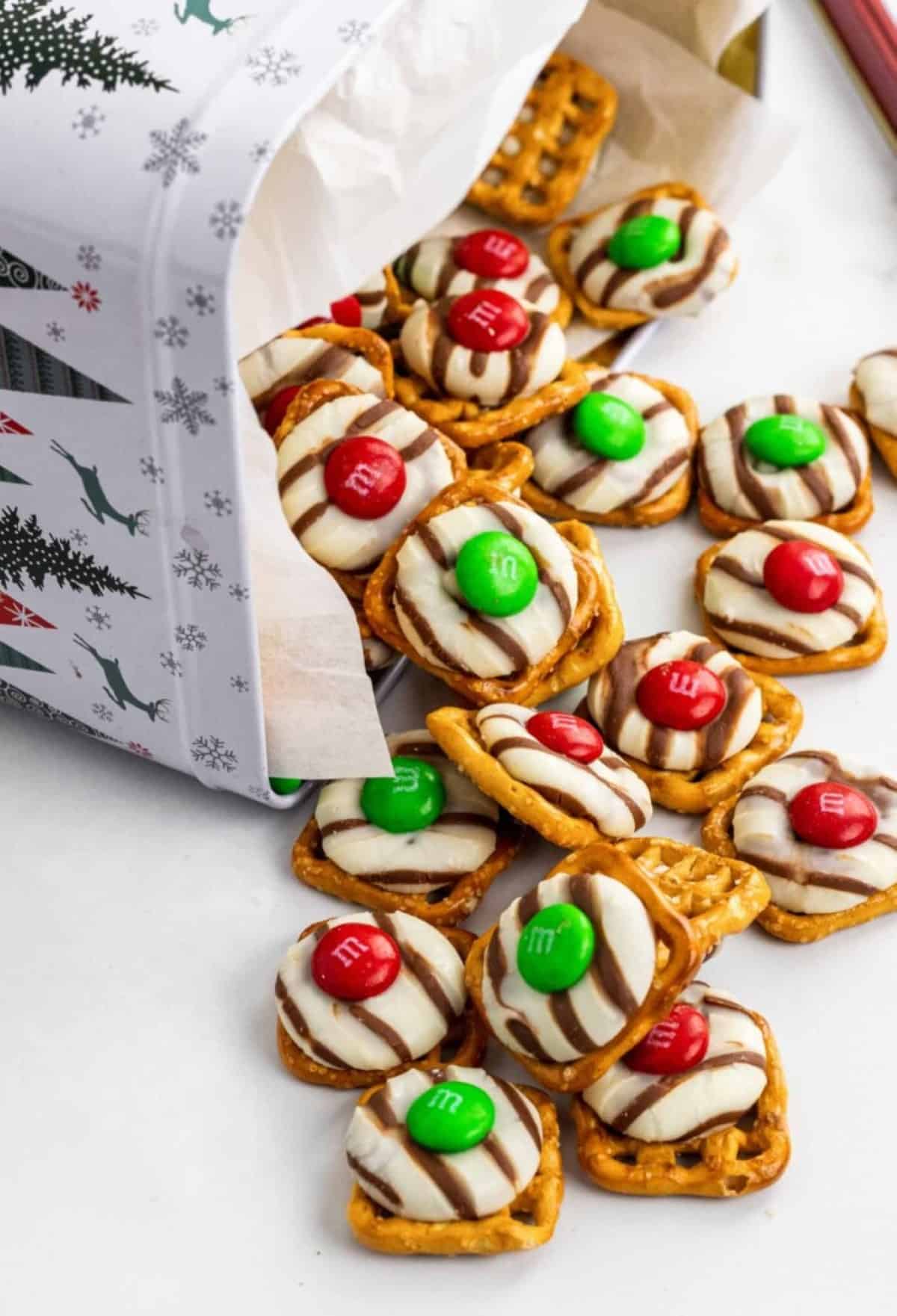 Christmas Pretzel Hugs spilling out of a Christmas tin on to a white countertop.