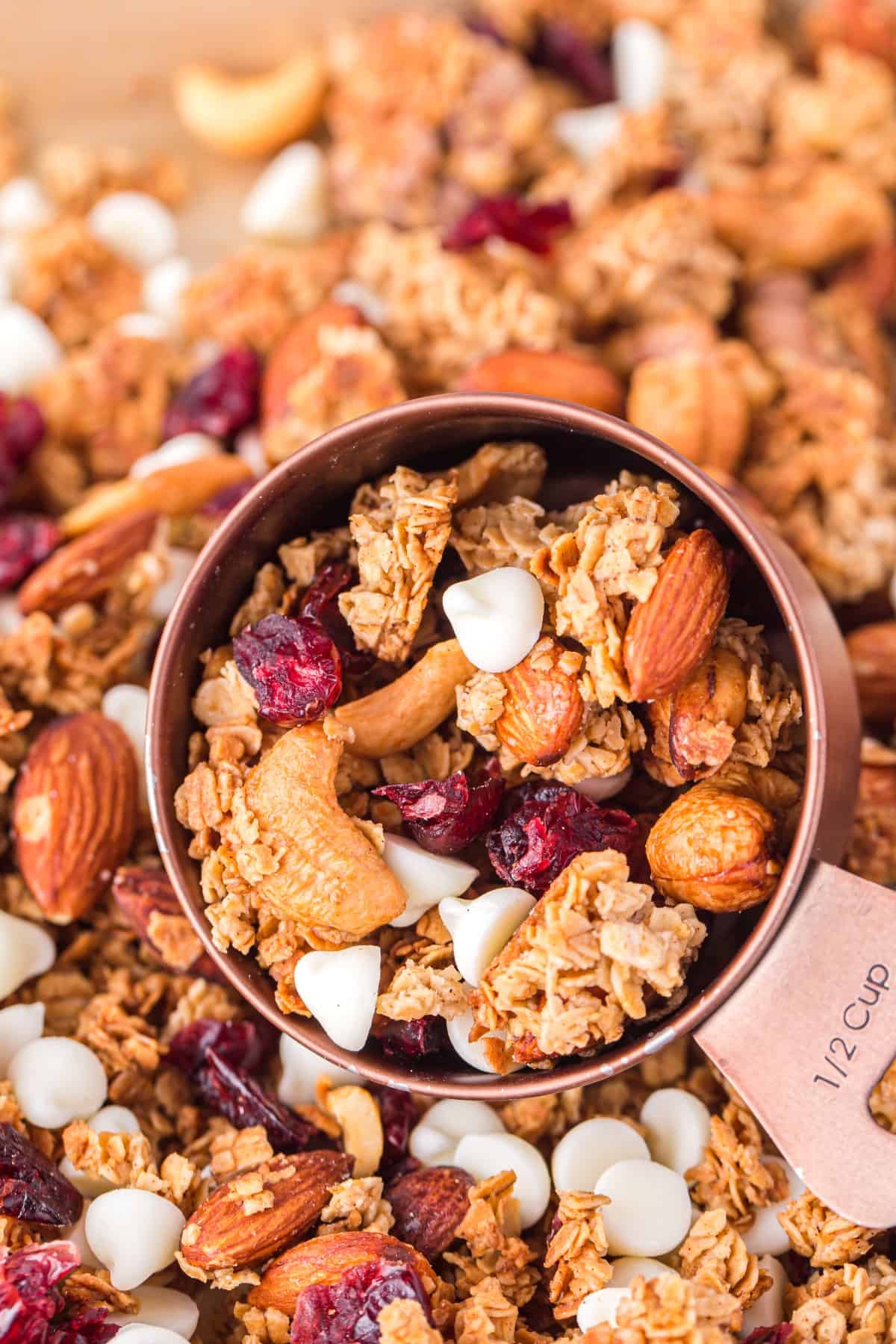 Close up of Christmas Granola: Cranberry White Chocolate in a measuring cup on a bed of granola. 