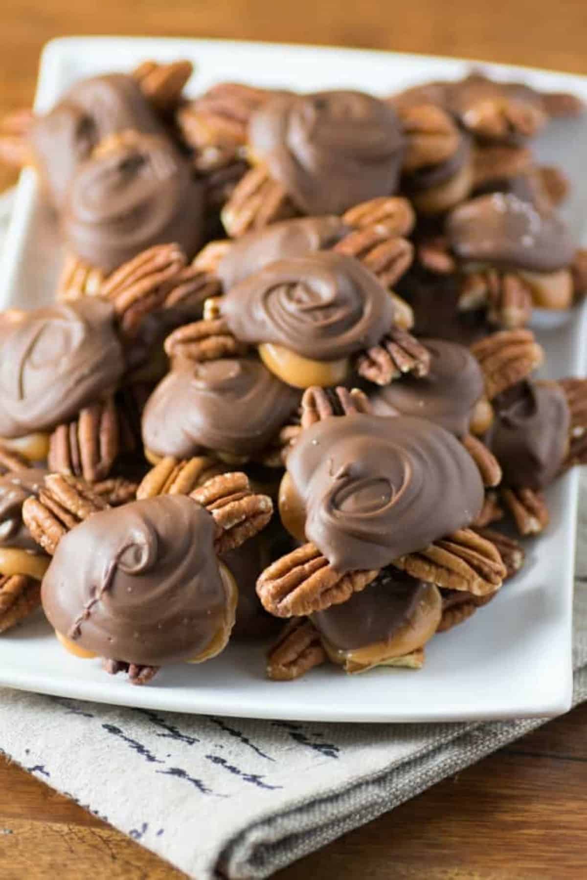 Homemade Chocolate Turtles stacked on a white plate.