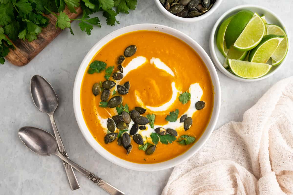 Horizontal photo of pumpkin soup topped with pepitas, coconut cream swirl and cilantro. 
