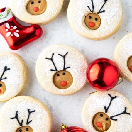 Overhead shot of Reindeer Linzer Cookies with red ornaments in between.