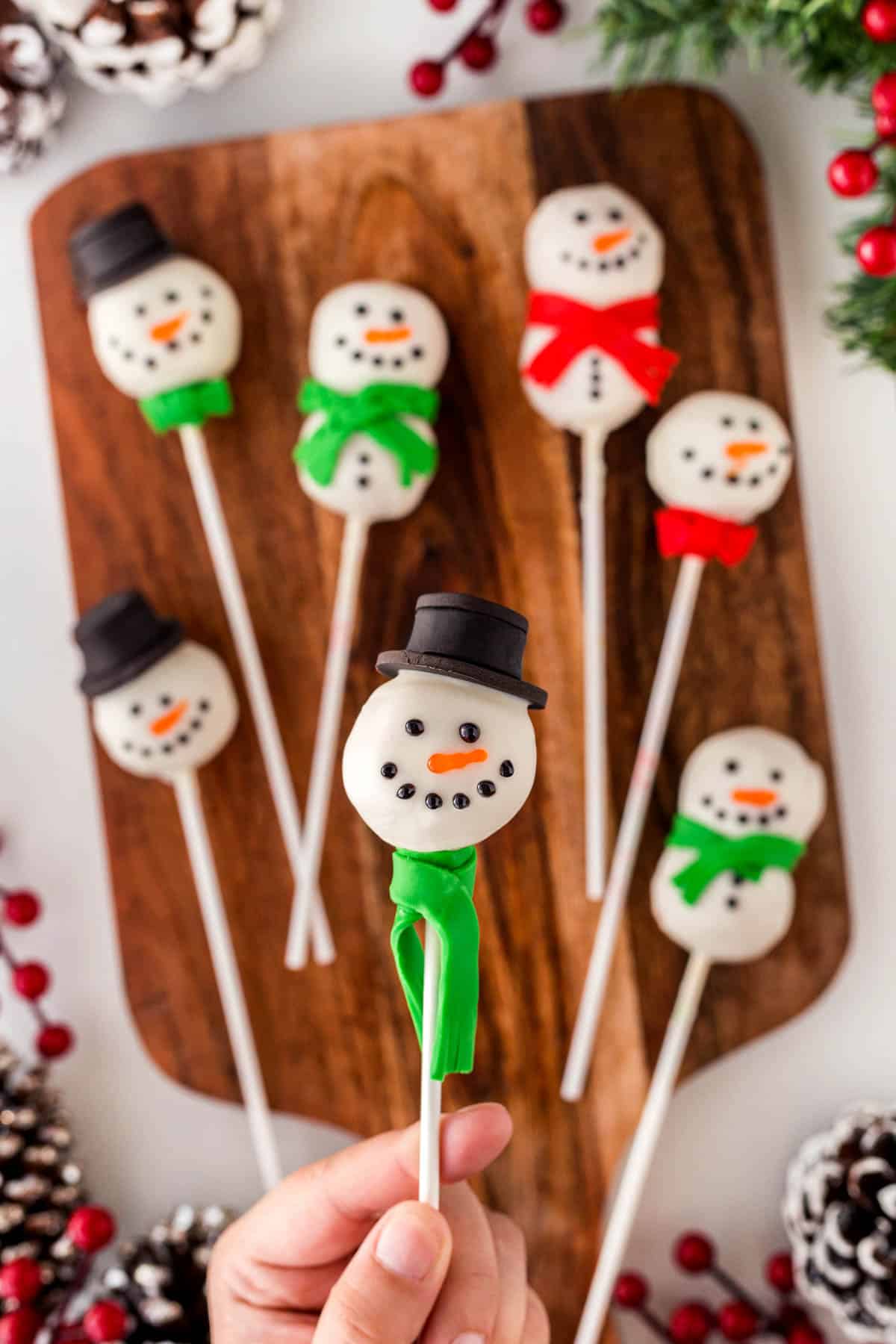Overhead shot of one Snowman Cake Pop close-up being held with more in the background on a board. 