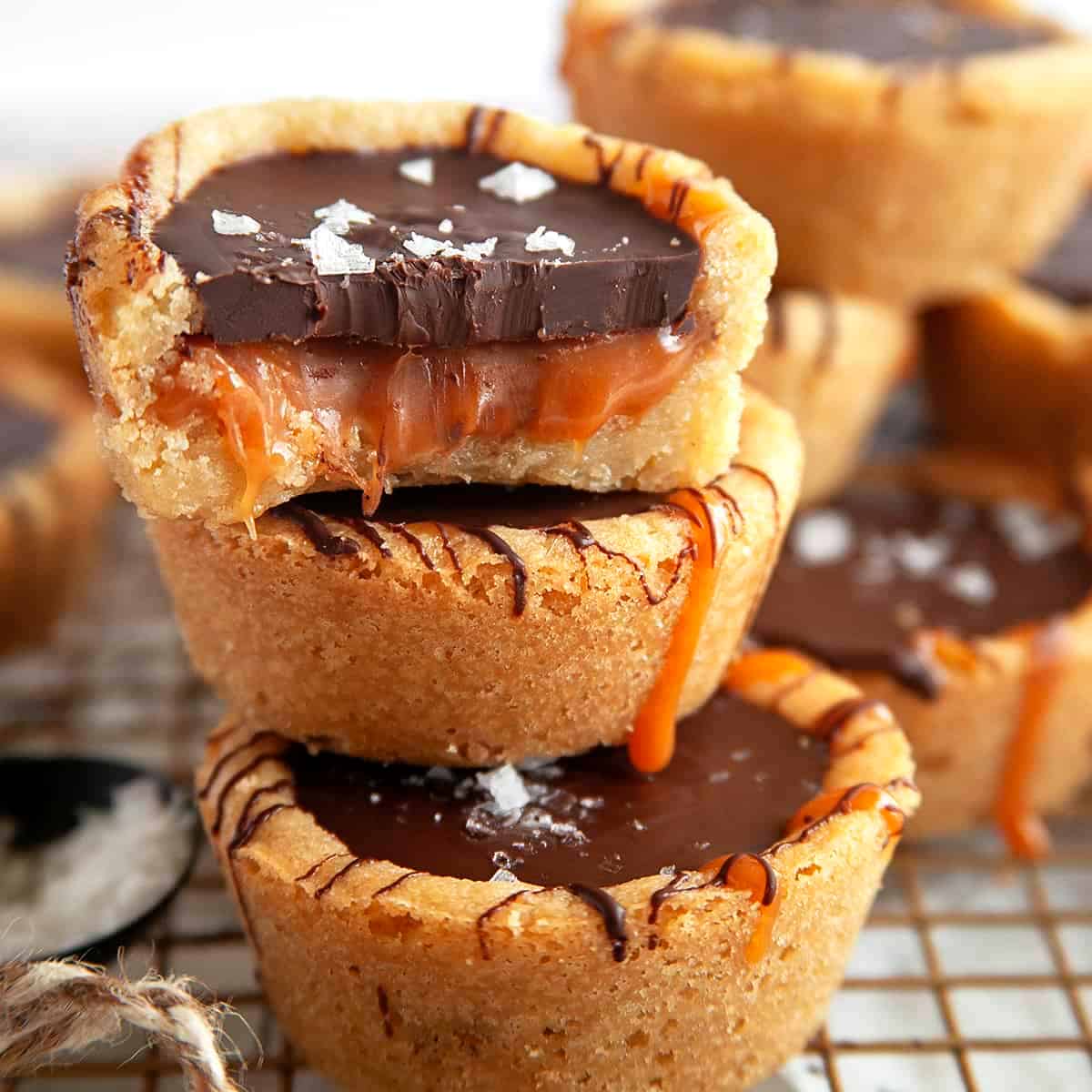 Stacked cookie cups with the top one has a bite taken showing ooey gooey caramel. 