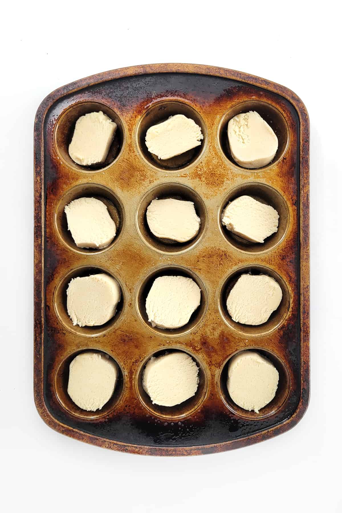 Sections of cookie dough in a muffin tin. 