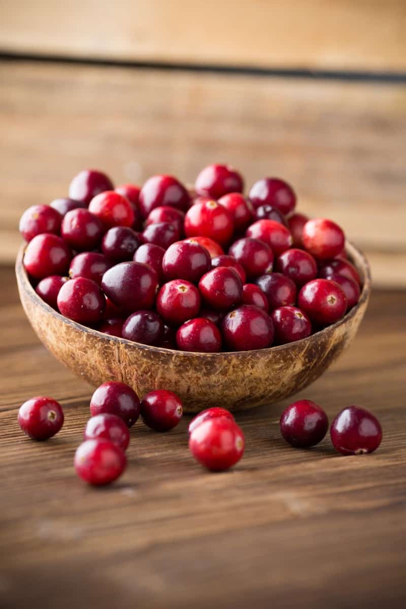 Cranberries in wooden bowl on wooden background.