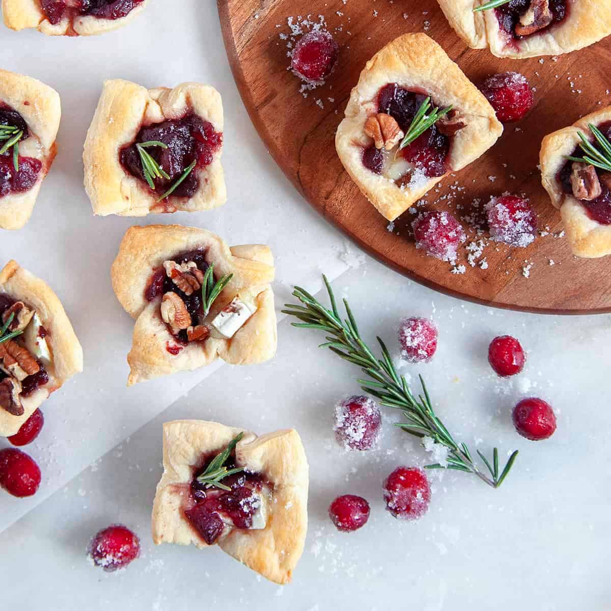 Overhead square image of Cranberry Brie Bites with scattered sugared berries and rosemary. 