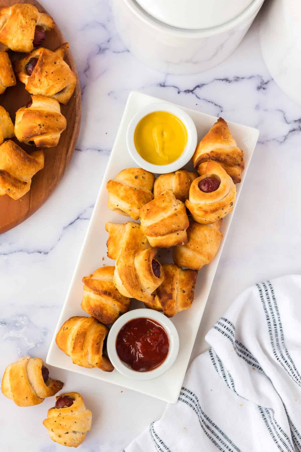 Overhead shot of pigs in a blanket on a serving platter with mustard and ketchup. 