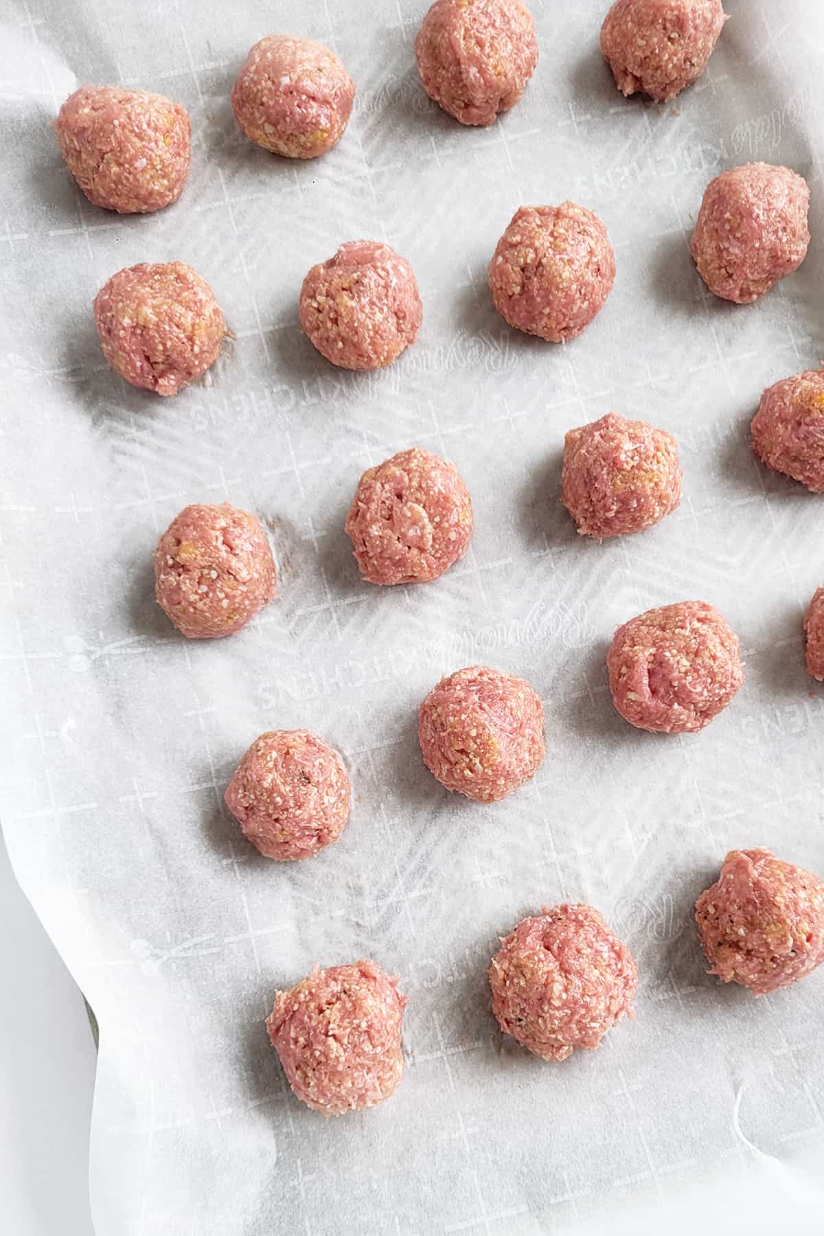 Sheet pan covered with parchment with chicken meatballs ready for the oven. 