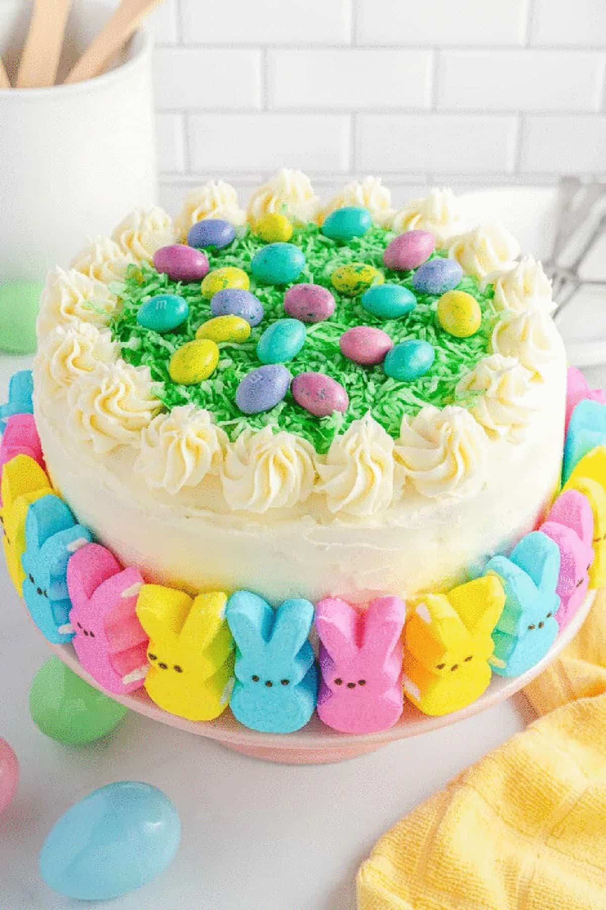 Easter cake decorated with eggs on top and Peeps around the bottom on the cake stand. 