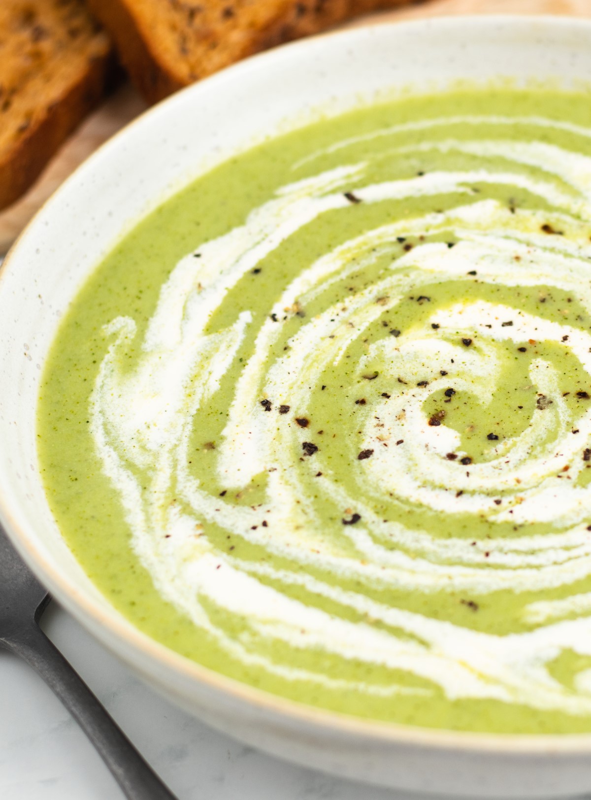 Close-up of broccoli soup with a cream swirl and fresh cracked pepper. 