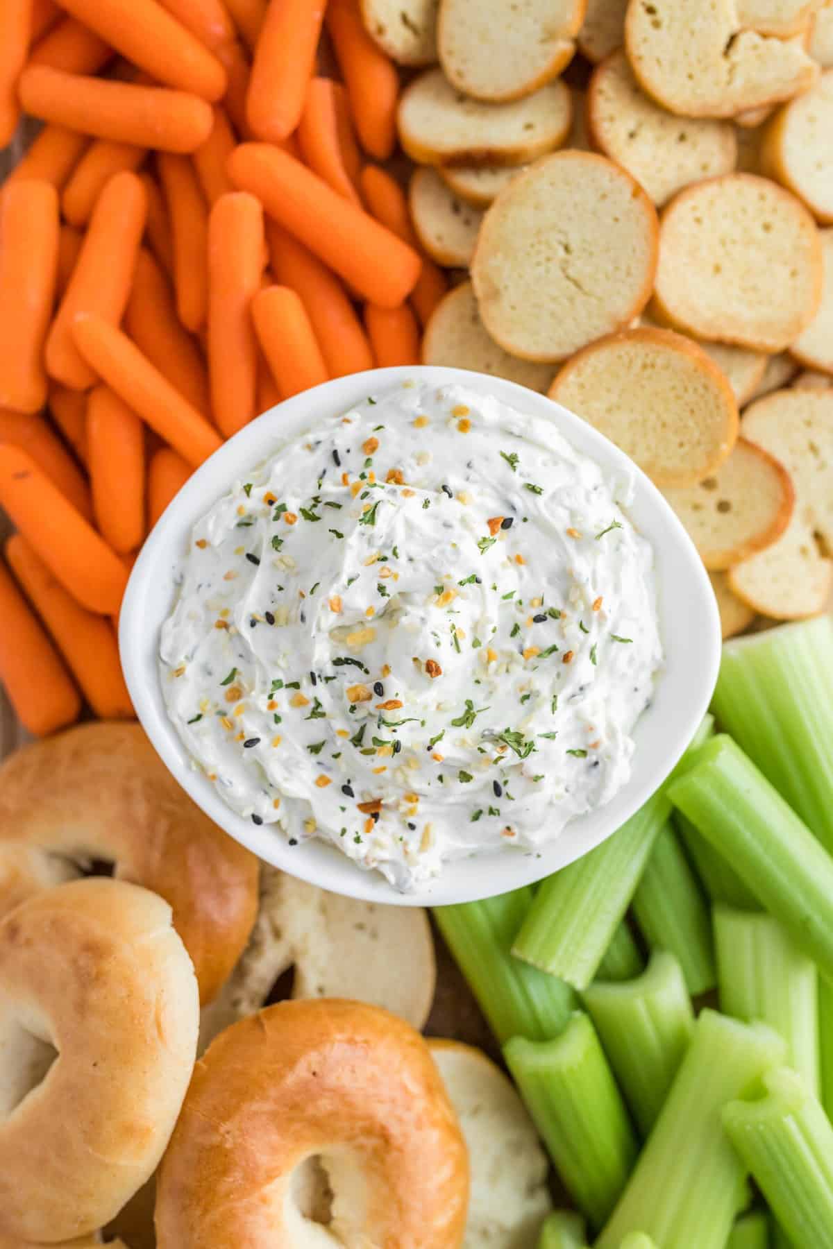 Overhead shot of the dip with carrots, celery, crostini and bagels close up. 