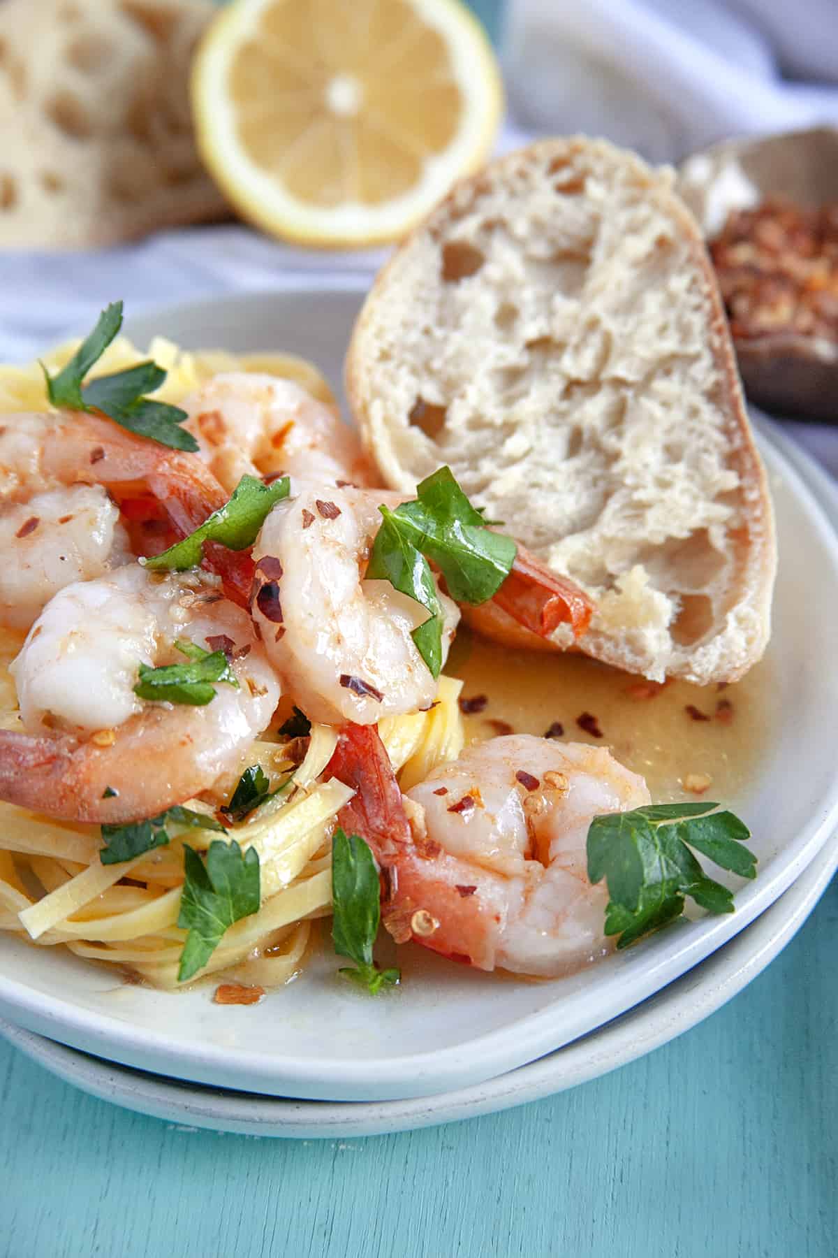 Vertical shot of shrimp scampi over pasta with crusty bread. 
