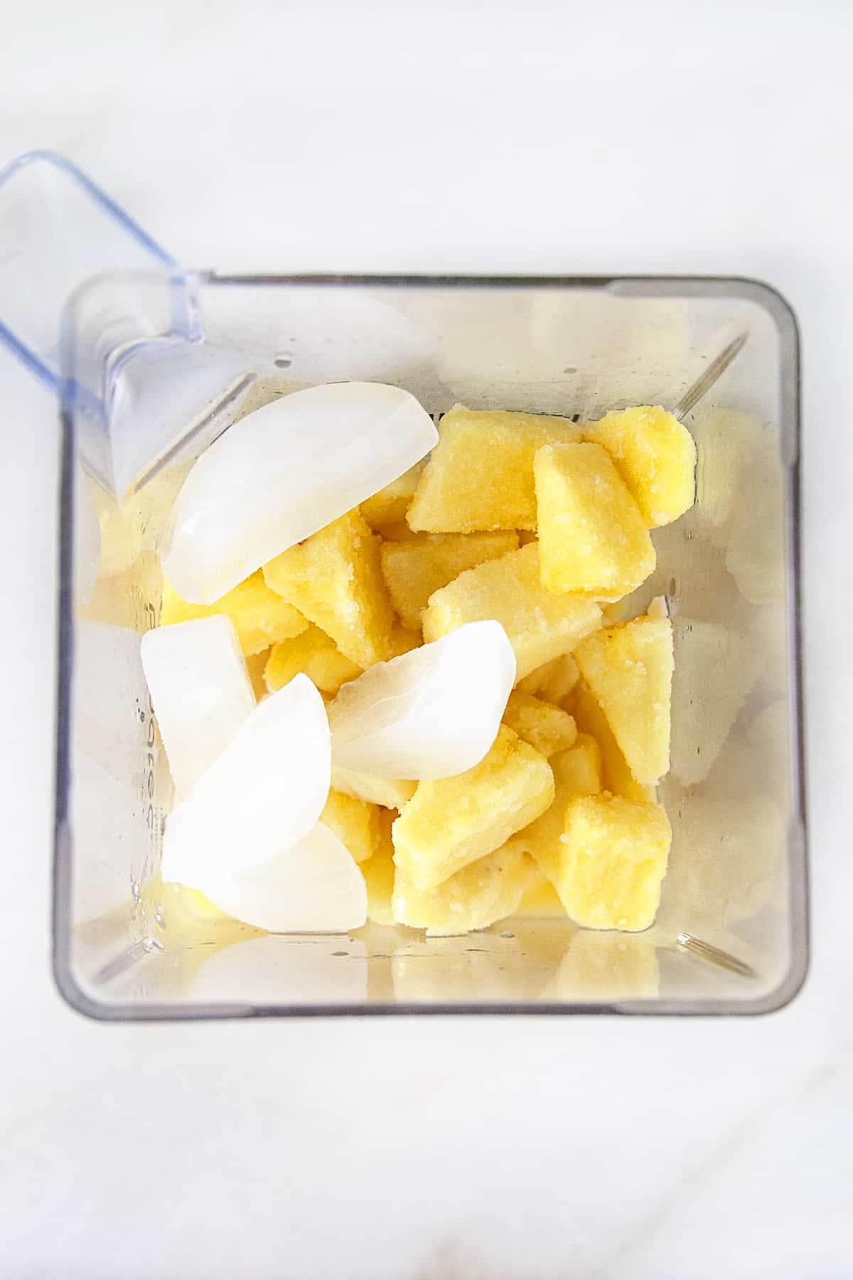 Looking into a blender filled with ice and frozen pineapple. 