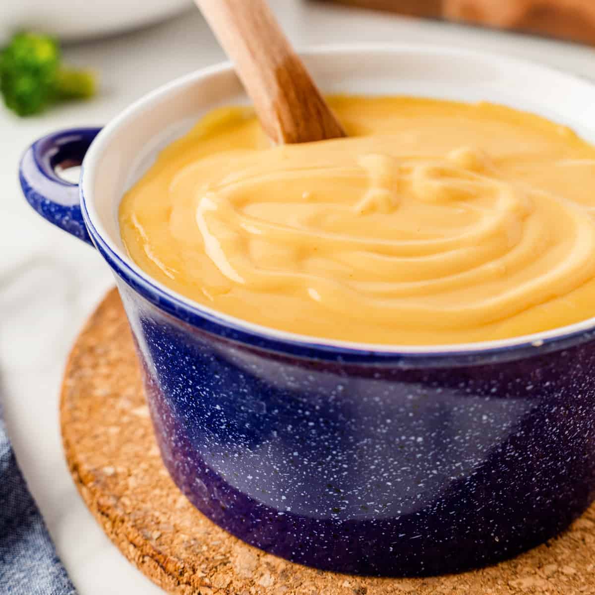 Square photo of cheese sauce in a blue serving pot. 