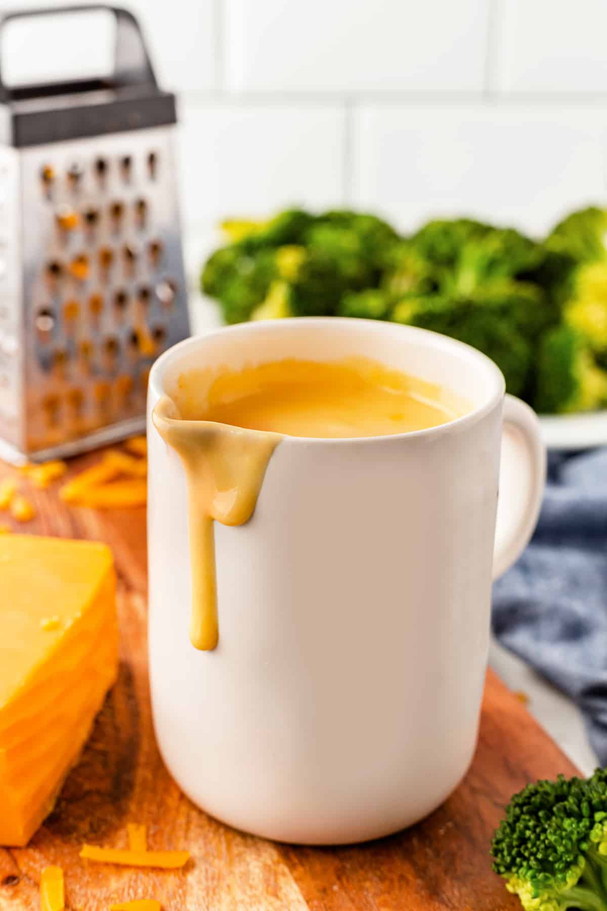 Cheese sauce in a tall white jug with drip of sauce.
