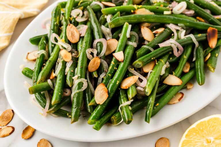 A plate of green beans garnished with sliced almonds and shallots.
