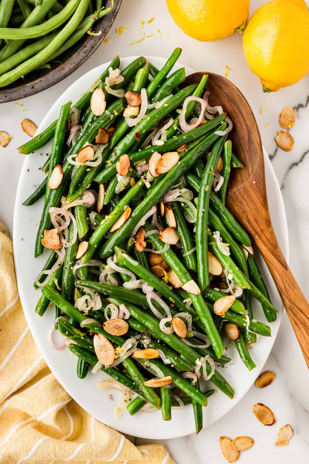 Close-up of green beans almondine on a platter with a wooden spoon. 