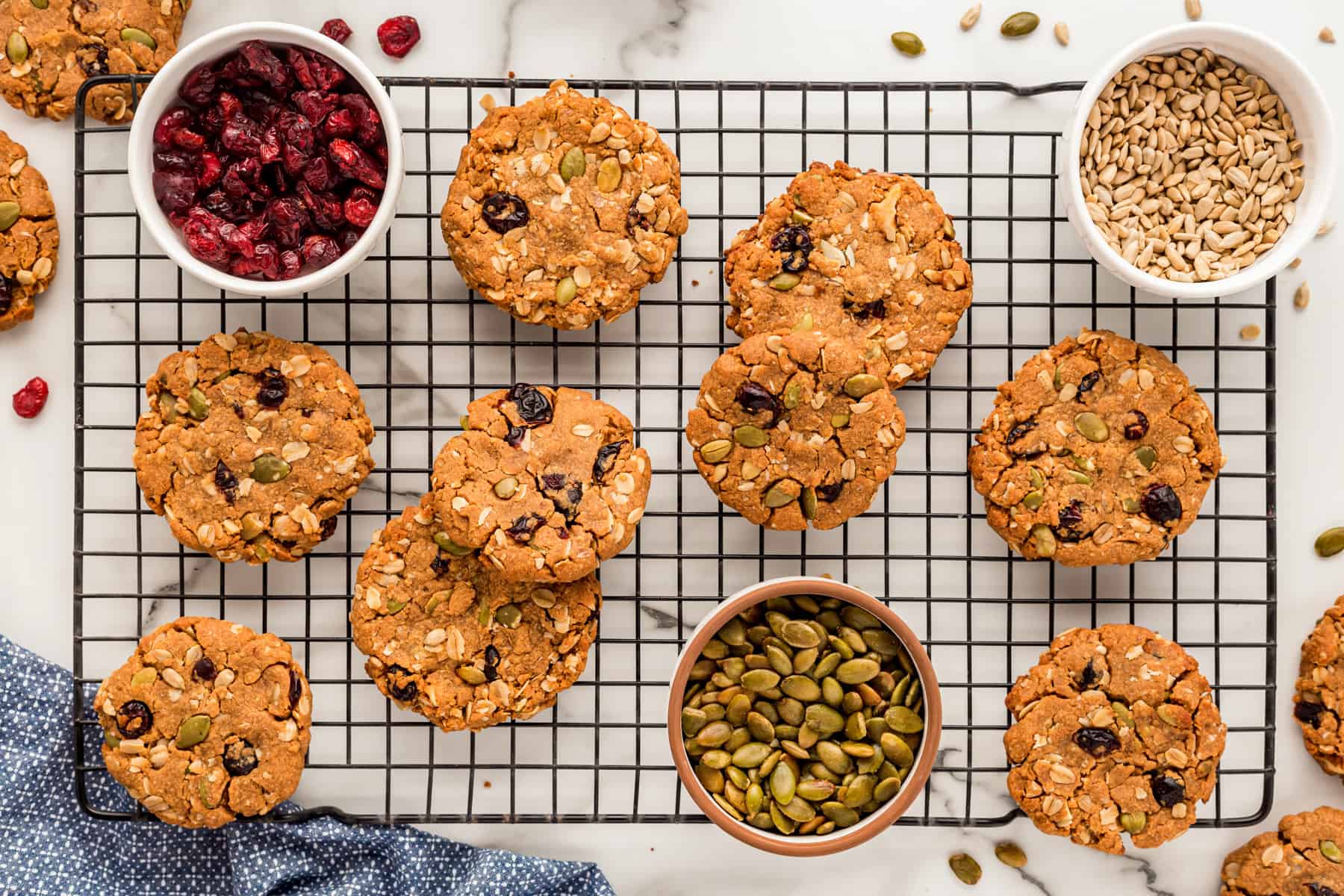 Horizontal picture of cookies with dishes of seeds and cranberries on a cooling rack. 