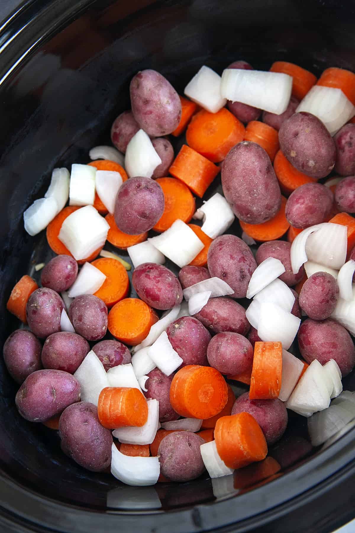 Potatoes, onions and carrots in a slow cooker. 