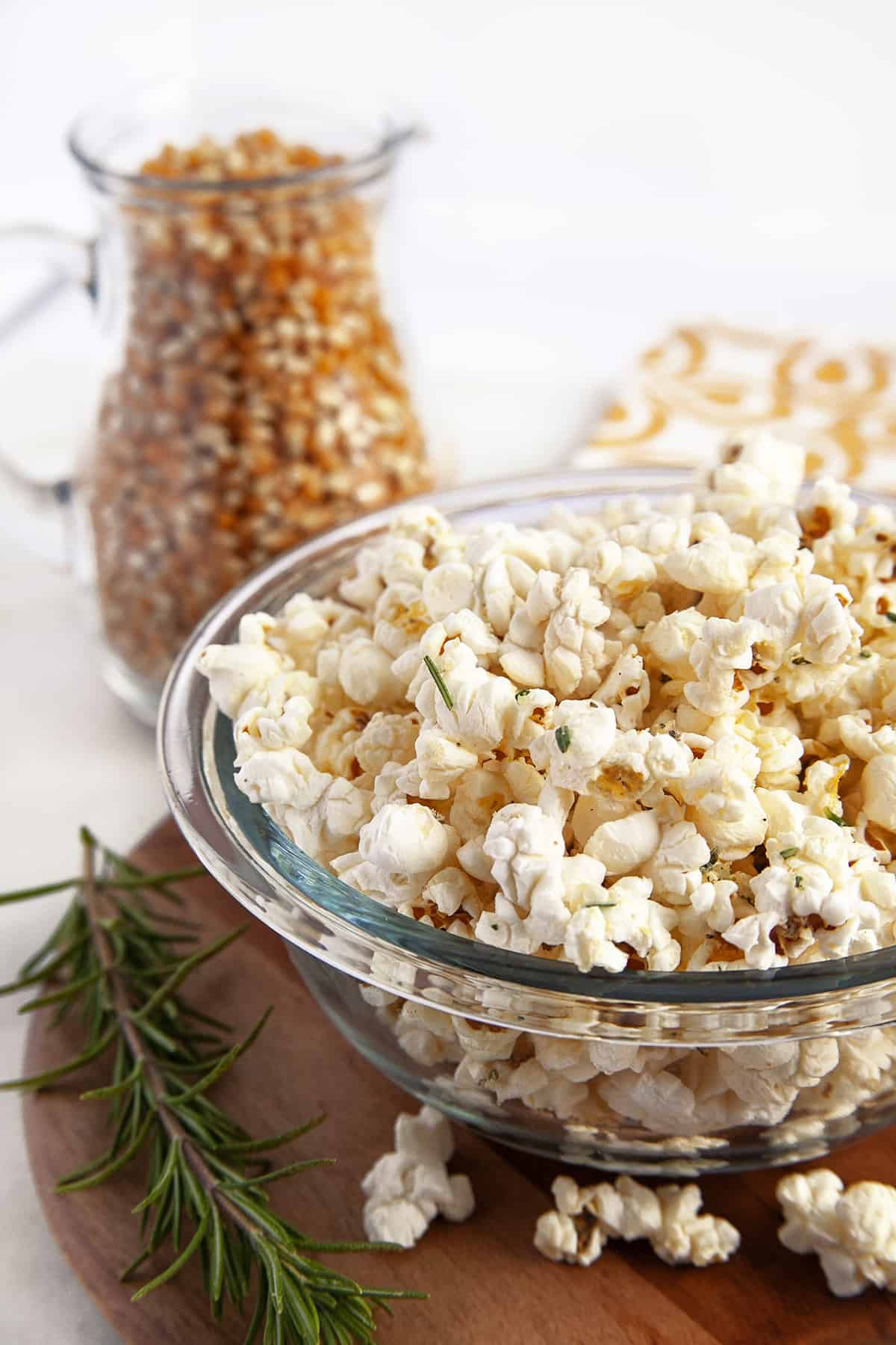 Popcorn in a glass bowl with kernels in a jar in the background. 