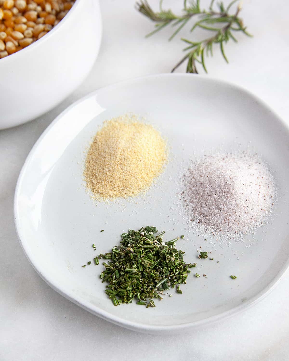 Garlic, salt and rosemary seasonings for the popcorn in small piles on a plate. 