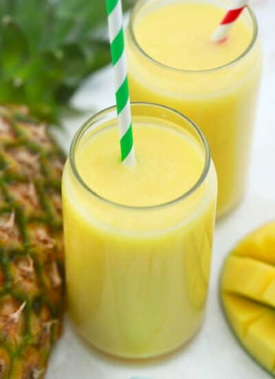 Large jar glasses of mango pineapple smoothie with straws.