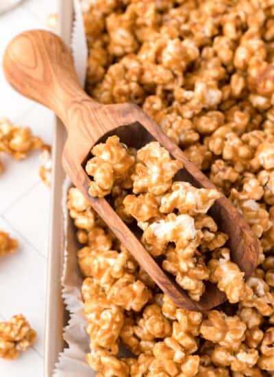 Close-up shot of caramel corn on a baking sheet with a small wooden scoop.