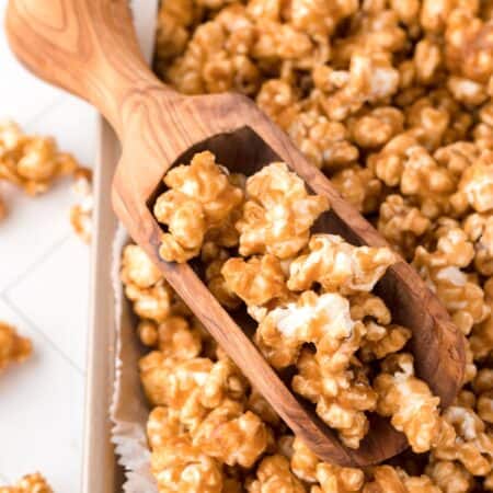 Close-up shot of caramel corn on a baking sheet with a small wooden scoop.