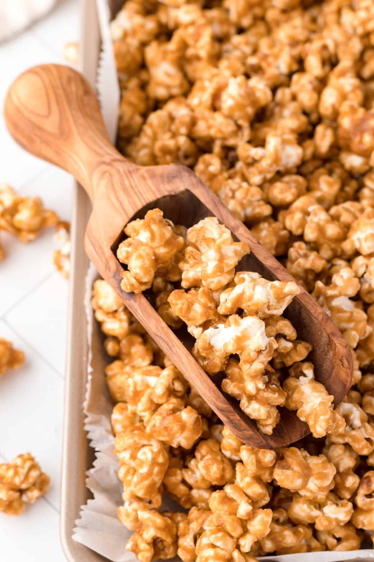 Close-up shot of caramel corn on a baking sheet with a small wooden scoop. 