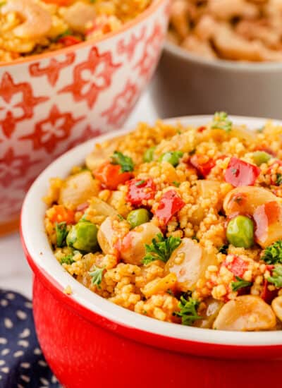 Moroccan Couscous in a red bowl with other bowls in the background.