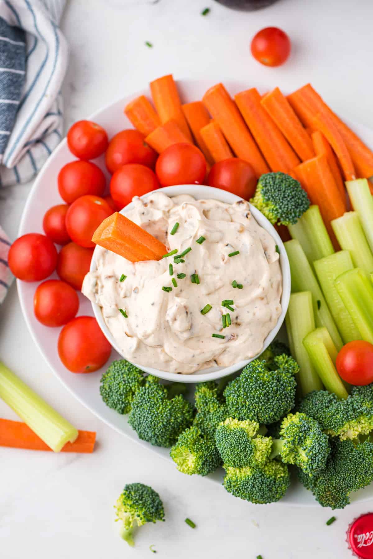 Dip with a carrot stuck in on a plateful of veggies. 